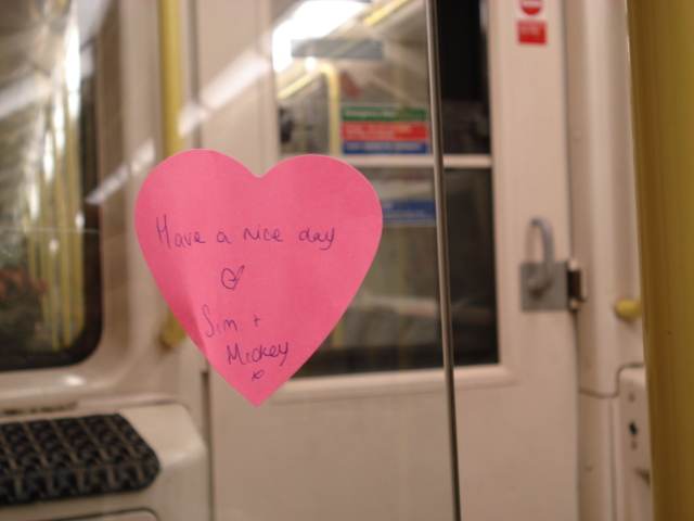 Image: A heart shaped pink post-it note stuck onto a window of a London tube train that reads"Have a nice day, heart, Sam and Mickey"